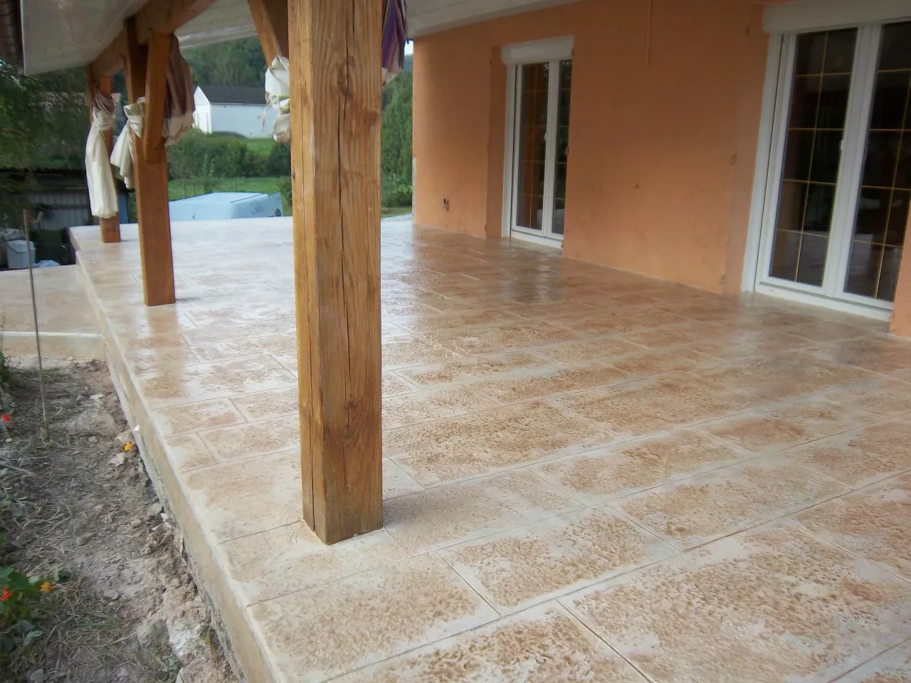 Terrasse couverte en béton imprimé façon dallage, tons sable, au pied d'une maison à façade orangée